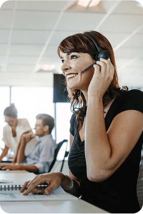 confident saleswoman speaking to client on headset in office with team members in the background