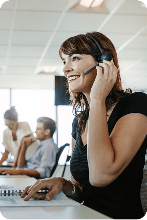 confident saleswoman speaking to client on headset in office with team members in the background confident saleswoman speaking to client on headset in office with team members in the background